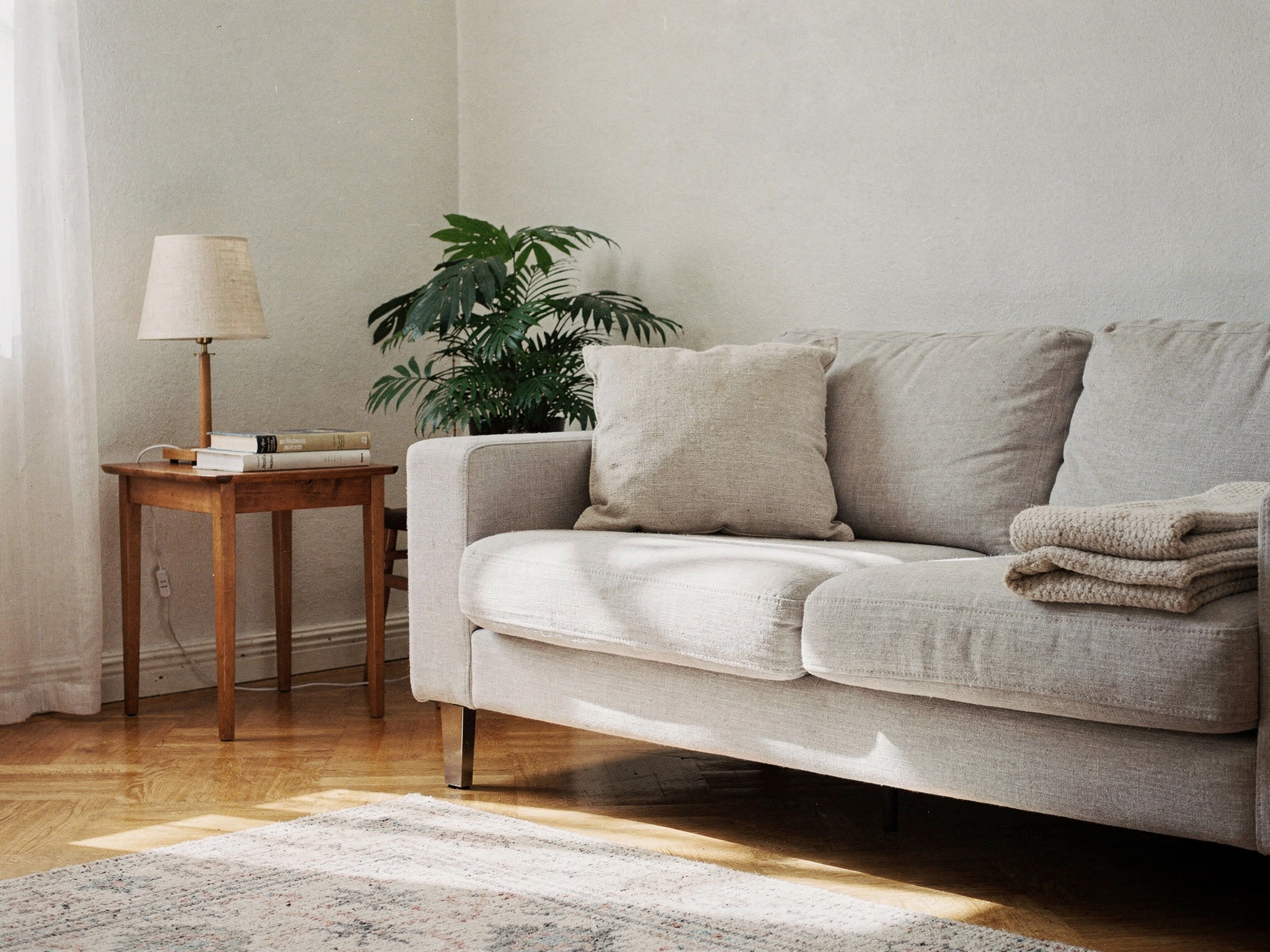 Soffhörna med kudde, hopvikt filt, sidobord med lampa och en dammsugen matta